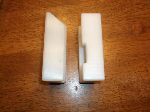 1995 Mercury Grand Marquis - Two white 3D printed objects are shown on a wooden surface. The object on the left is a rectangular prism with an angled top. The object on…