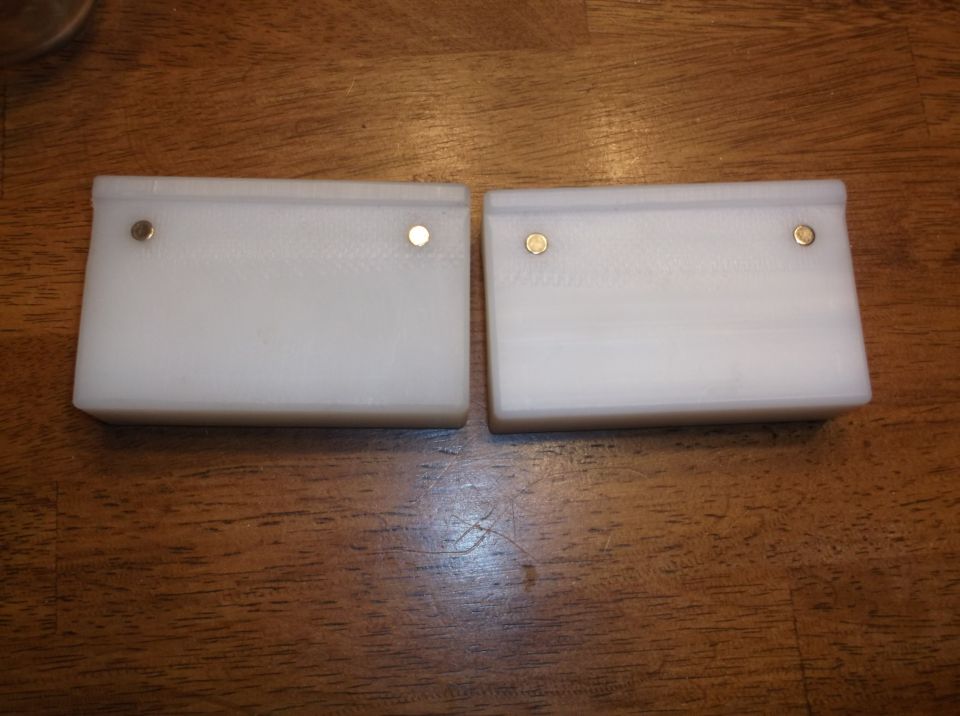 Two white rectangular objects with brass pins on a wooden surface.