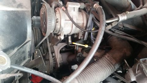1985 Ford Bronco - The image shows a close-up view of an engine bay, focusing on the air conditioning compressor and associated belts and hoses. A yellow dips…