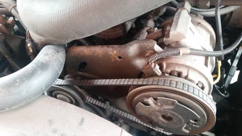 1985 Ford Bronco - The image shows a close-up view of an engine bay, focusing on the serpentine belt system and an air conditioning compressor. A large, ribbe…