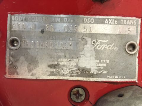 1965 Ford Mustang - A close-up of a metal data plate affixed to a red vehicle. The plate contains various alphanumeric codes and text, including "Ford" brandin…