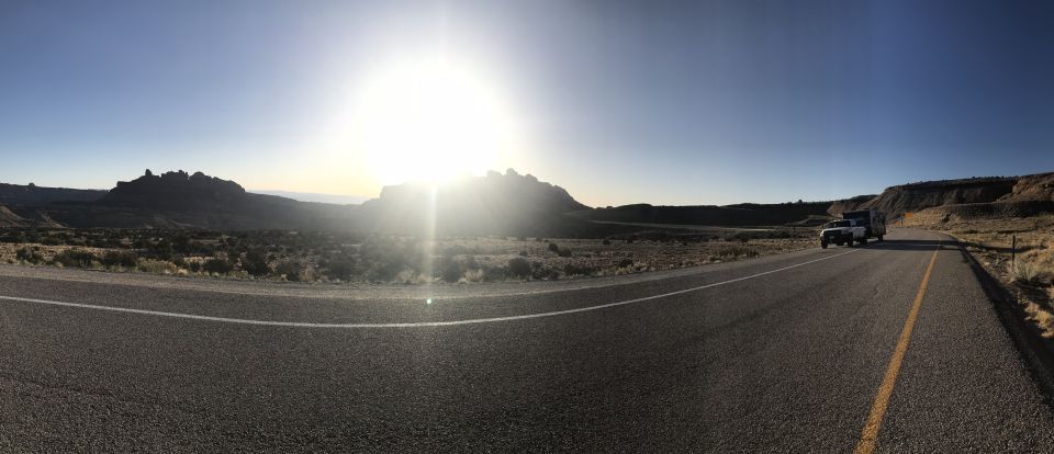 White pickup truck towing a trailer on a highway in a desert landscape.