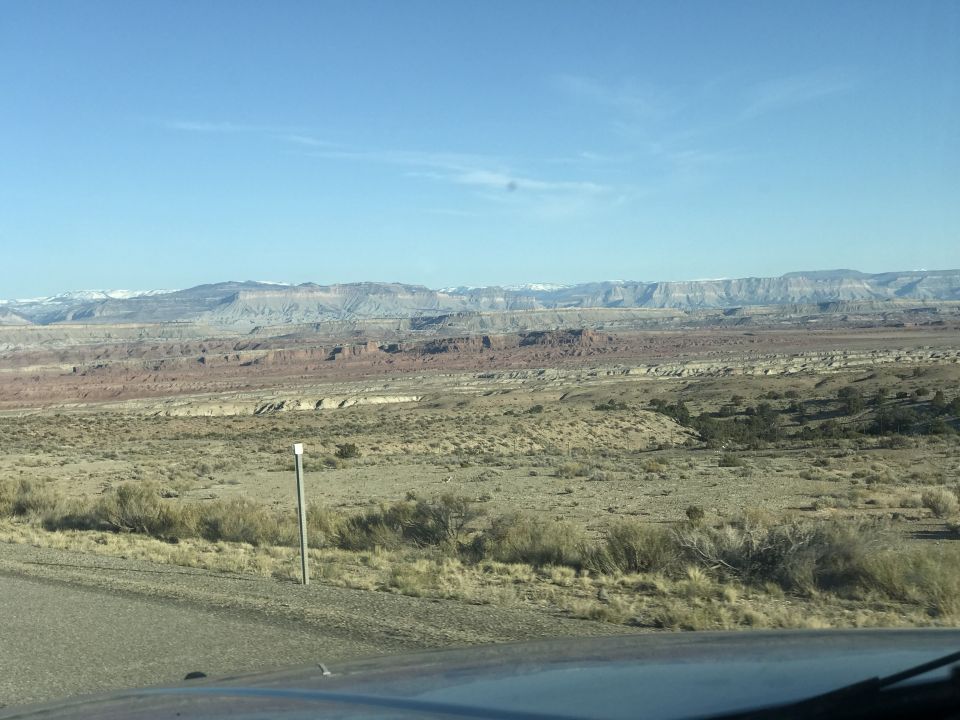 Desert landscape with layered rock formations and sparse vegetation.