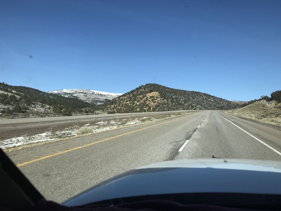 Highway through mountains with snow on peaks and roadside.