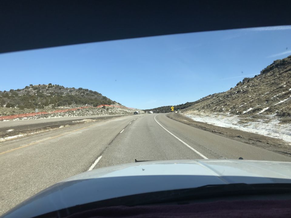 View from inside a vehicle driving on a highway with hills and some snow on the sides.