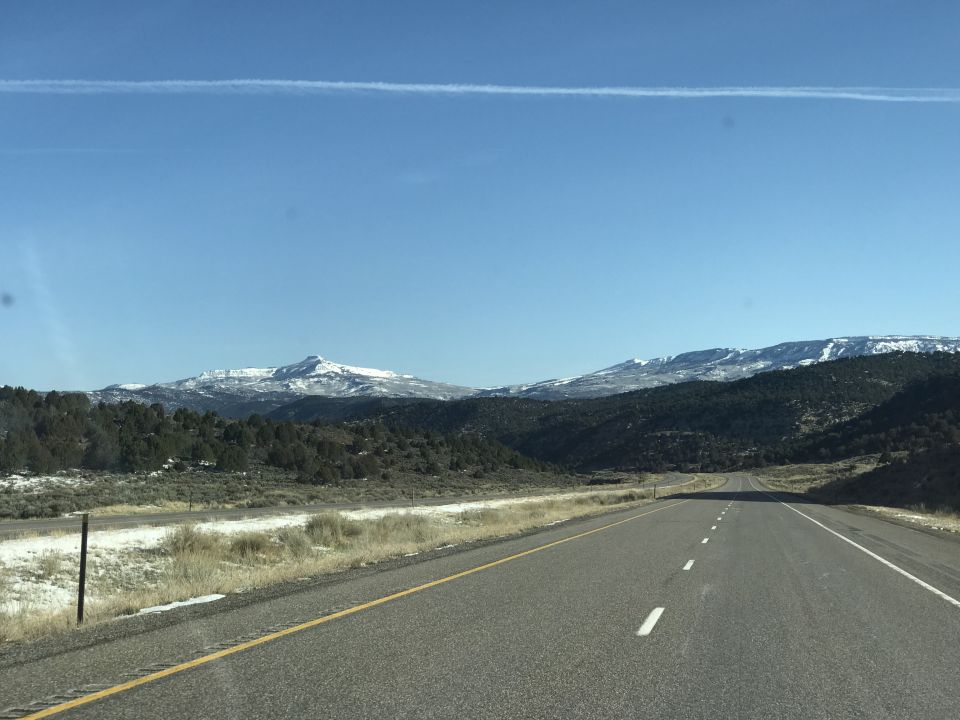 Road leading towards snow-capped mountains under a clear blue sky.