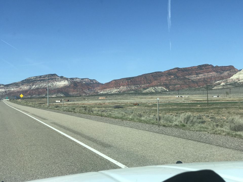 Highway leading towards red and white layered mountains in a desert landscape.
