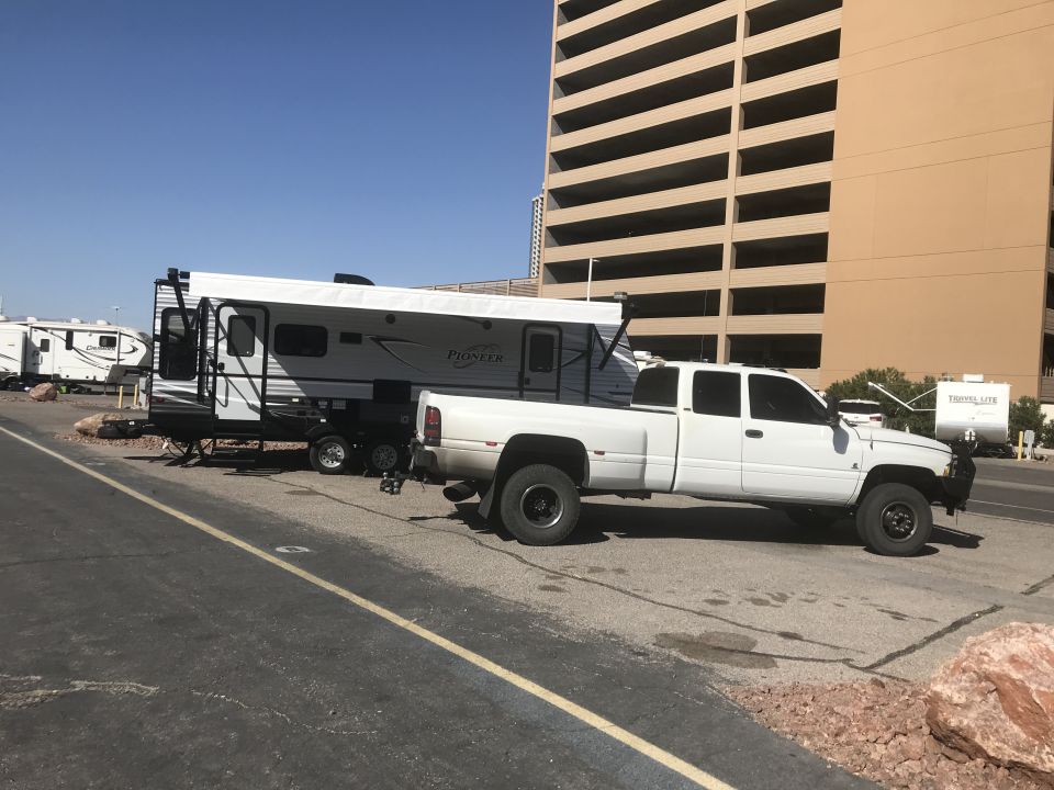 White dually pickup truck towing a white travel trailer with "Pioneer" branding.