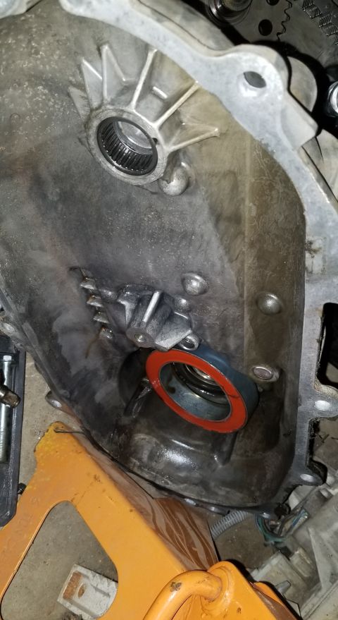 1995 Ford Bronco - A close-up view of a transmission housing with a new seal being installed. The metal housing shows signs of wear and some fluid residue.