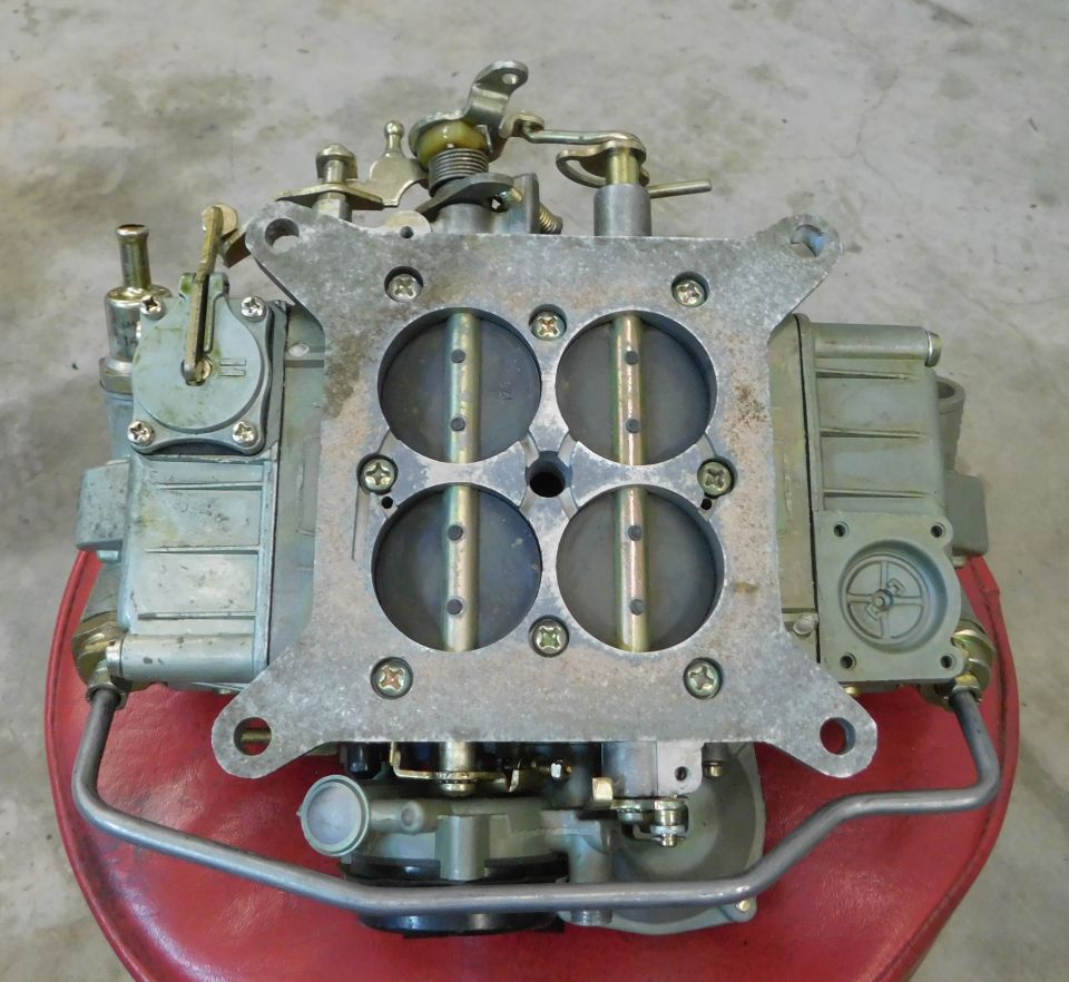 Top view of a four-barrel carburetor with silver metal body and visible linkages.