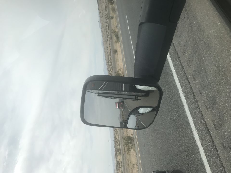 Side mirror reflecting a red truck on a highway.