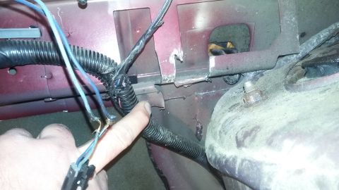 2000 Pontiac Grand Prix - A hand points to damaged electrical wiring with exposed copper near a corrugated plastic conduit. The wiring is attached to the red painted…