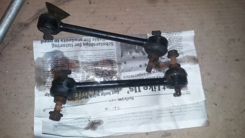2000 Pontiac Grand Prix - Two black sway bar end links with rusty bolts are laid out on a piece of newspaper on a concrete floor.