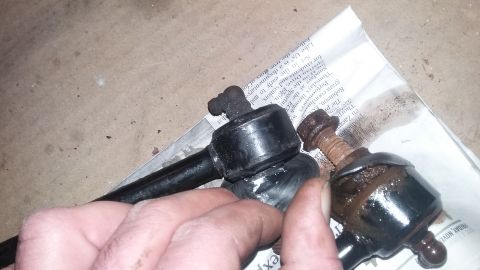 2000 Pontiac Grand Prix - A person's hand holds two automotive suspension stabilizer links, one appearing newer and black, the other older and rusted, resting on a p…