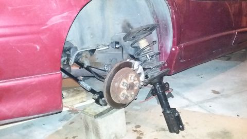 2000 Pontiac Grand Prix - The rear suspension of a red Pontiac Grand Prix is disassembled. The wheel hub, brake rotor, and shock absorber assembly are visible, with…
