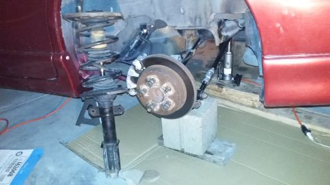 2000 Pontiac Grand Prix - The image shows the suspension system of a red car, likely a 2000 Pontiac Grand Prix, undergoing maintenance. A strut assembly is visible i…