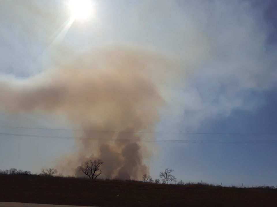Smoke plume rising into the sky with silhouetted trees and a hill.