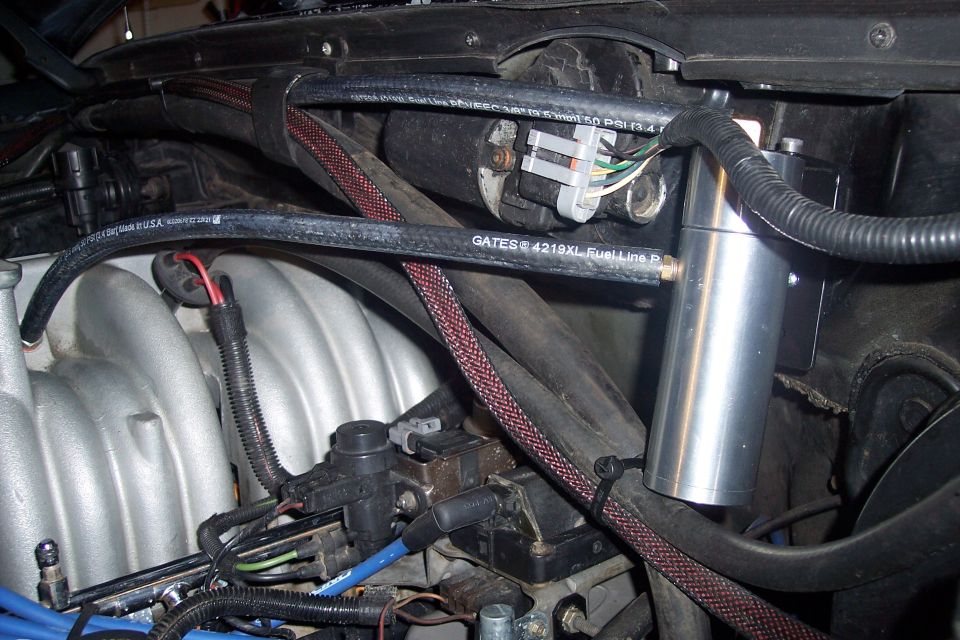 Engine bay of a 1995 Ford Bronco with fuel lines, wiring, and an aluminum canister.