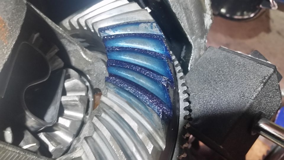 Now its time to run a pattern on the gearset.  Mark the ring gear with marking paint.  Marking paint comes in different colors, including yellow and blue.  Blue is easier to see on shiny gears, and yellow is easier to see on dark gears.  Since NAPA only had "Prussian Blue", that's what I used here.

Once marked, run the ring gear around several times in both directions.  The contact with the pinion gears will squeeze out the marking paint and leave a faint pattern that we'll use to see how the ring gear comes in contact with the pinion gear.  This will tell us whether the pinion depth is set correctly, and whether the ring gear will need to move to one side or another.

What you see in the pic is the "coast" side.  Again, I used all the shims that came with the original housing.  This pattern is satisfactory--hell, its pretty damned near perfect, although the lighting could reflect it better.

Keep in mind that any oil residue on the gearset will make reading the pattern much more difficult.  Get it as clean as you can.