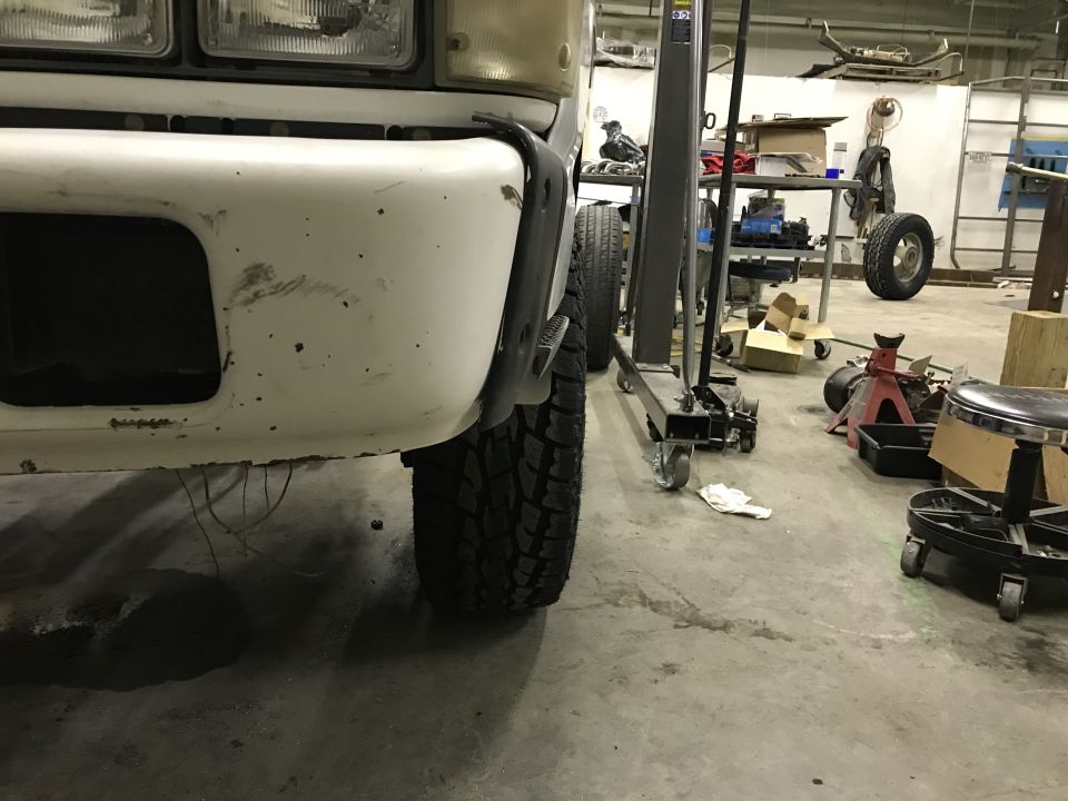 White Chevrolet C/K pickup truck front bumper and tire in a workshop.