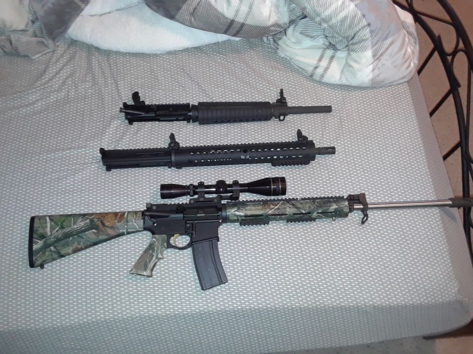 Three disassembled AR-15 uppers and one complete rifle on a bed.