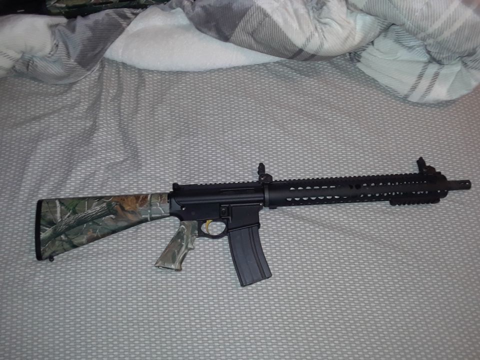 Rifle with camouflage stock and grip on a bed.