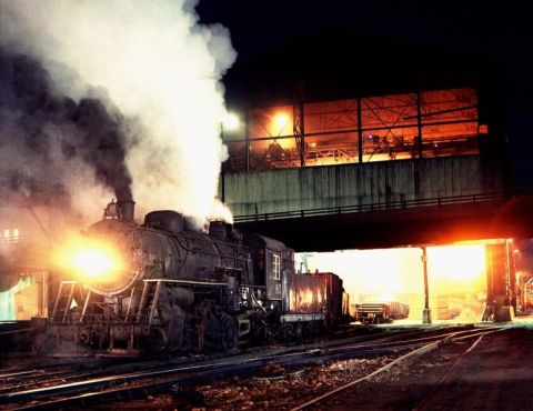 1967 Ford Custom Wagon - A steam locomotive at night emits thick smoke and steam, illuminated by its bright headlight and the warm glow of industrial lights in the…
