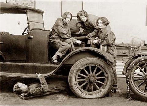 1967 Ford Custom Wagon - Three women in work clothes pose with a vintage car. One woman is lying underneath the car as if working on it, while two others sit in the…