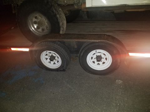 1968 Ford Bronco - A flat tire on a white trailer is visible, with the wheel of a vehicle on the trailer in the background. The trailer has orange reflective…