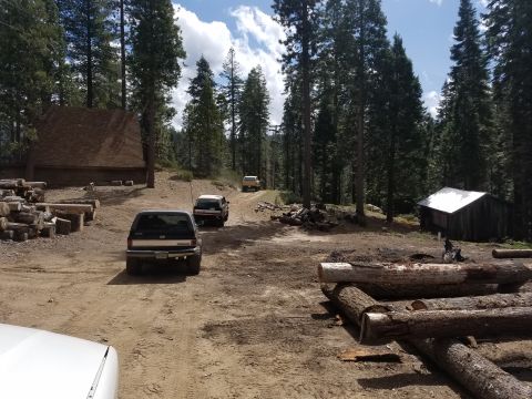 1968 Ford Bronco - Three SUVs drive down a dirt road surrounded by tall pine trees. A large wooden building is visible on the left, and a smaller wooden shed…