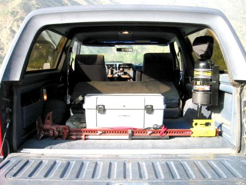 1985 Ford Bronco - The cargo area of a vintage Ford Bronco contains camping and recovery gear, including a cooler and a Hi-Lift jack.