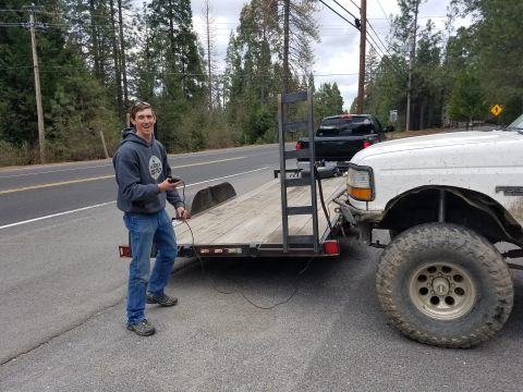 1968 Ford Bronco - A man in a gray hoodie and jeans stands next to a flatbed trailer and a white pickup truck. The man is holding a black remote control, and…