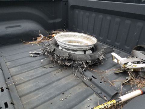 1968 Ford Bronco - The bed of a pickup truck contains a damaged tire and rim, along with a ratchet strap and other miscellaneous items.