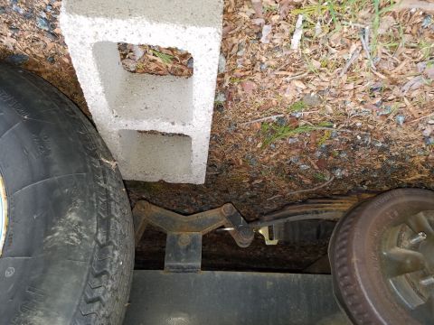 1968 Ford Bronco - A cinder block rests on the leaf spring of a trailer axle, next to a tire. The trailer frame and a rusty brake drum are also visible.