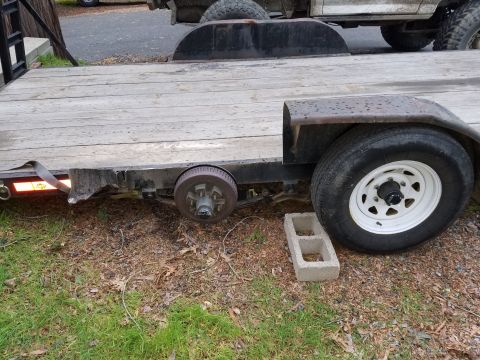 1968 Ford Bronco - A close-up side view of a flatbed trailer with a damaged fender and a missing tire on the left side. A concrete block is placed near the re…