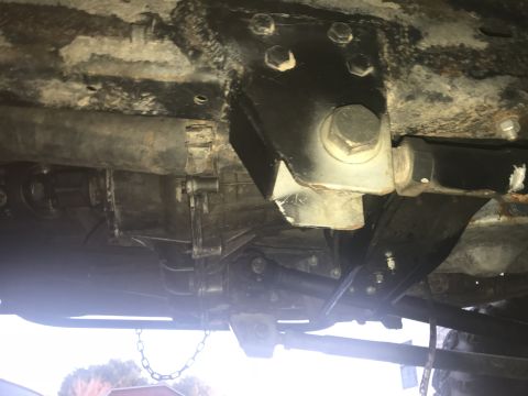 1989 Ford Bronco - The underside of a vehicle shows a transfer case and driveshaft assembly, with a large black metal bracket bolted to the frame above.