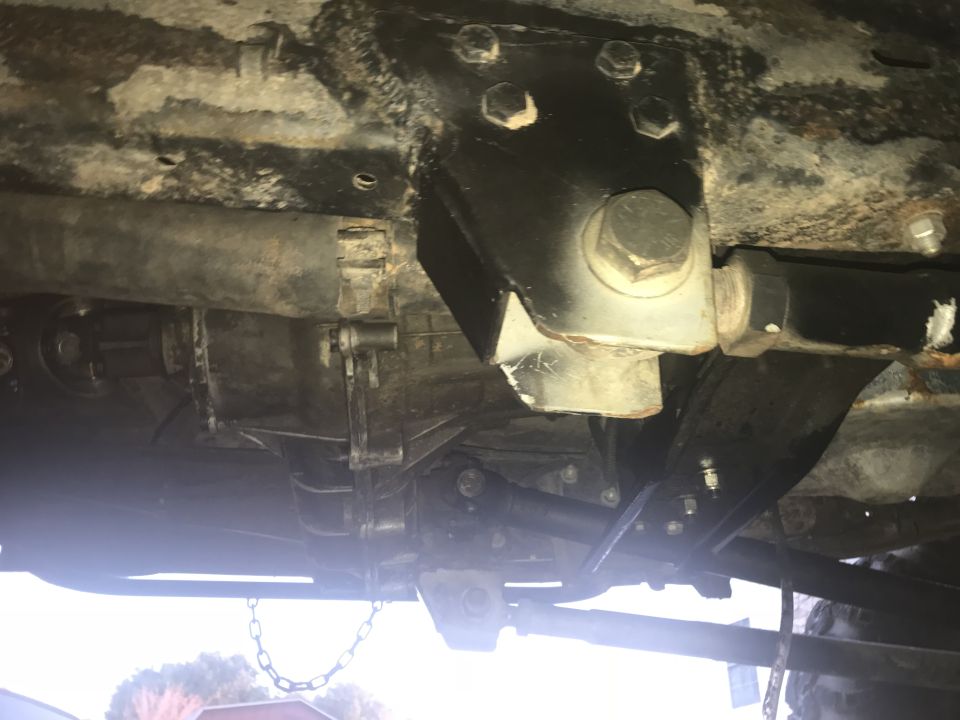 Underside view of a vehicle's drivetrain with a transfer case, driveshaft, and custom bracket.