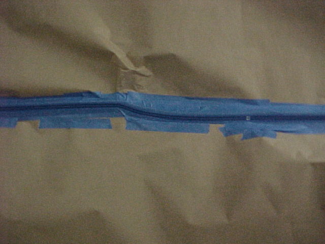Blue painter's tape masking a thin pinstripe line between brown paper on a car body