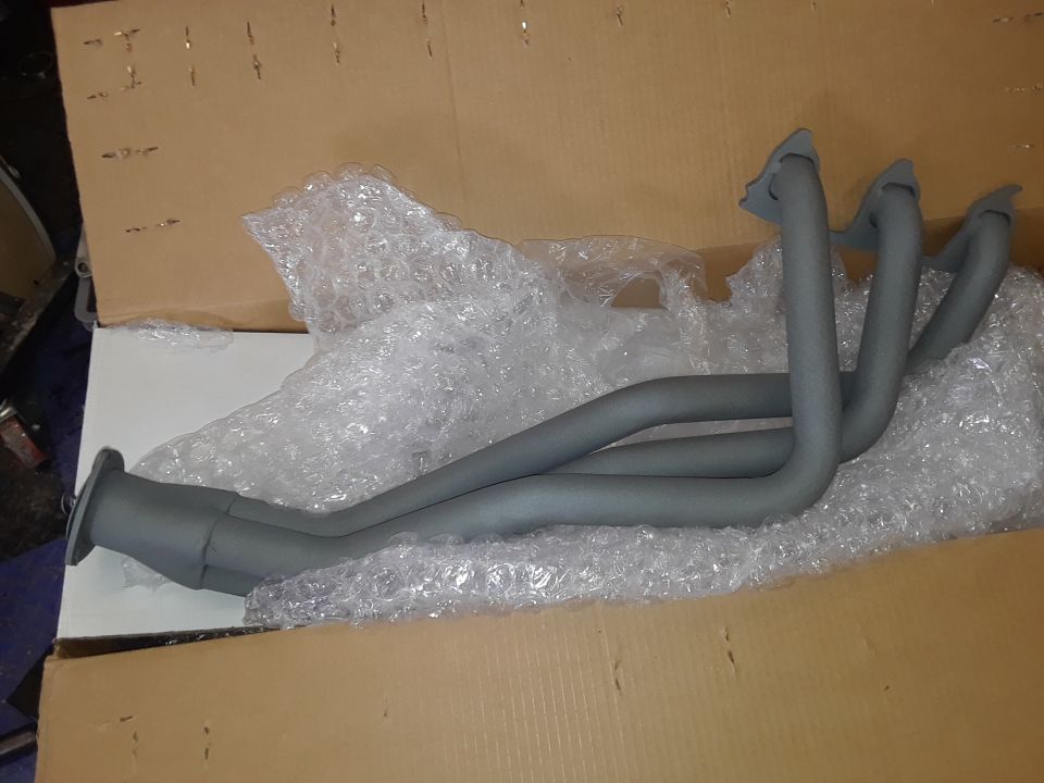 Grey exhaust headers in bubble wrap inside a cardboard box.