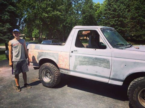 1996 Ford Bronco - A white 1996 Ford Bronco is shown from the front-three-quarter angle, with a person standing next to the driver's side door.