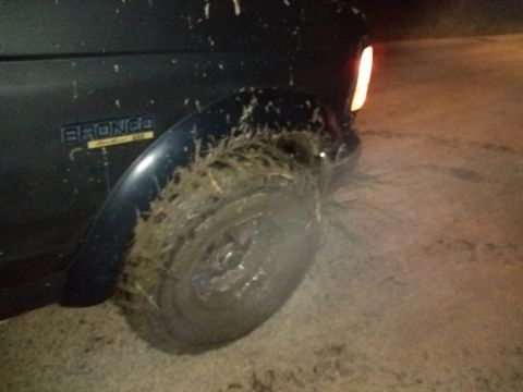 1996 Ford Bronco - Close-up of a dark SUV's rear tire and fender, seen at night.