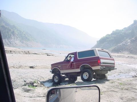 1988 Ford Bronco - Ford Bronco navigating a rough, dry riverbed with mountains in the background. Another vehicle is seen in the distance.