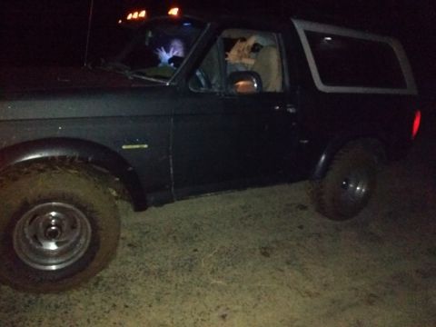 1996 Ford Bronco - A dark Ford Bronco is seen from the front-left at night, with mud on its tires.