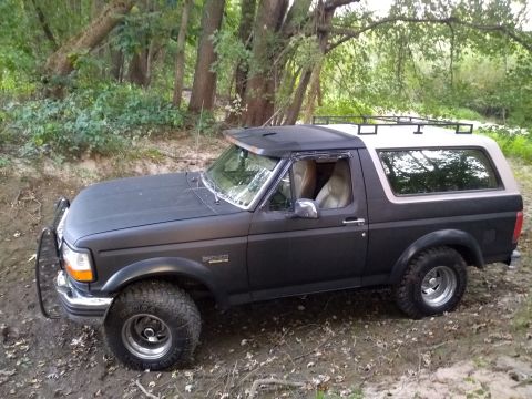 1996 Ford Bronco - A Ford Bronco is parked off-road with trees and foliage surrounding it.