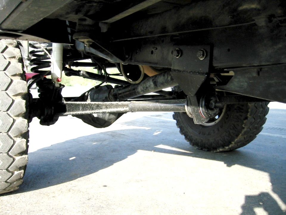 Undercarriage of lifted 4x4 showing front axle, steering linkage and off-road tires