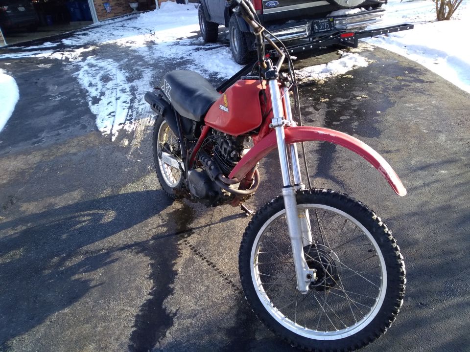 Red Honda dirt bike parked on a wet driveway with snow.