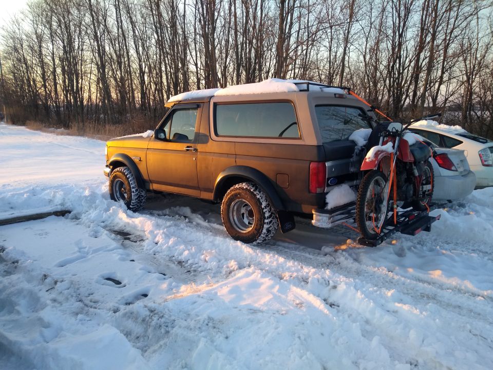 Bronco in snow with dirt bike on rear rack, another car parked nearby