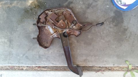 1985 Ford Bronco - A weathered clutch pedal assembly, showing signs of rust and wear, rests on a concrete surface.