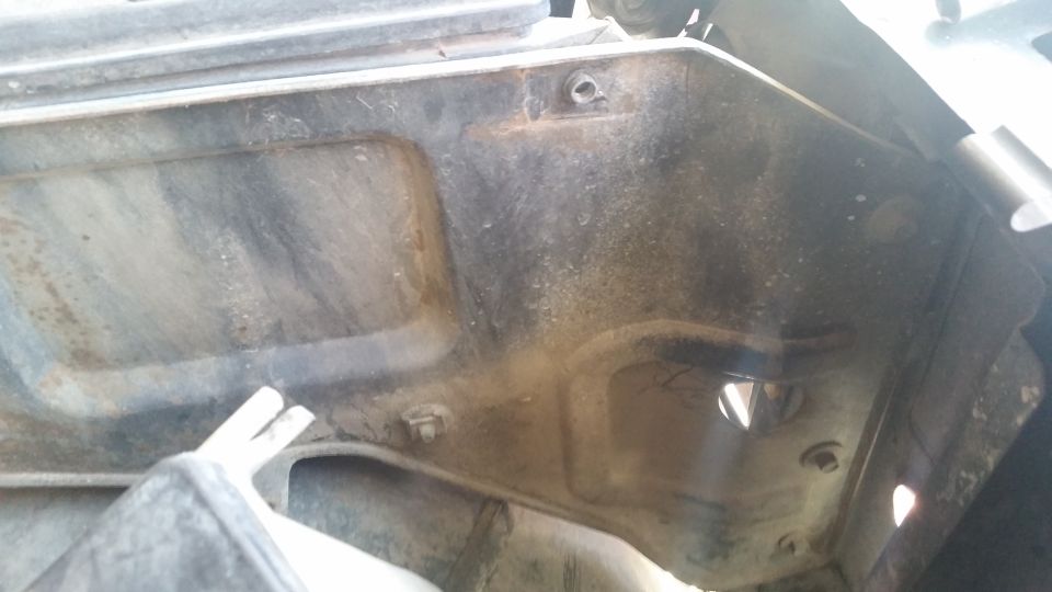 Close-up of the underside of a vehicle's hood, showing some metal bracing and a few bolts. Some hoses or wires are visible at the bottom