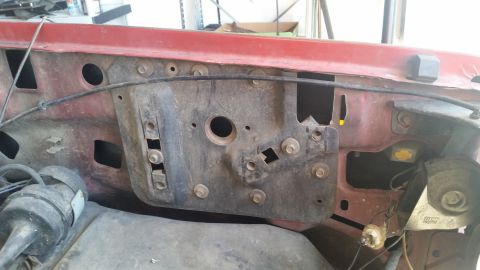 1985 Ford Bronco - The firewall and engine bay of a red vehicle, with visible bolts and openings, suggests a model year around 1980.